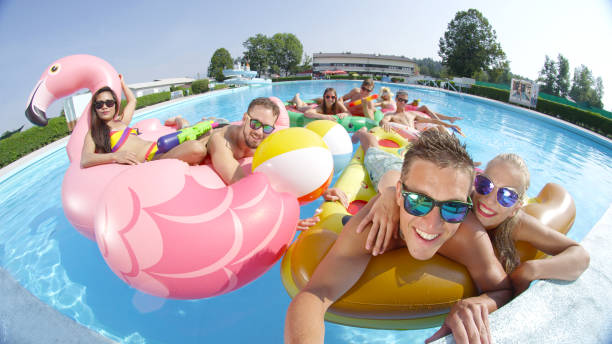 SELFIE: Cheerful happy friends making selfie on fun colorful floaties in pool SELFIE CLOSE UP PORTRAIT: Happy smiling friends doing selfie while having water-gun fight on fun colorful floaties in pool. Young people on inflatable flamingo, pizza, watermelon and doughnut floats hot filipina women stock pictures, royalty-free photos & images