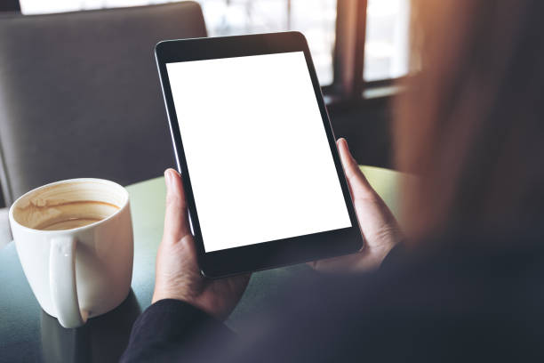 istock Mockup image of hands holding black tablet pc with blank white screen and coffee cup on table in cafe 951105788