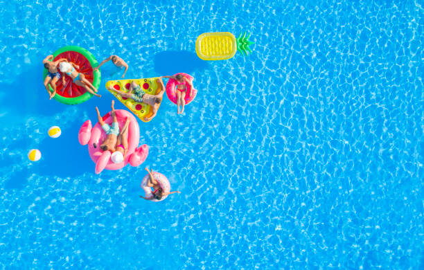 aerial: group of happy attractive people hanging out on fun floaties in the pool - float imagens e fotografias de stock