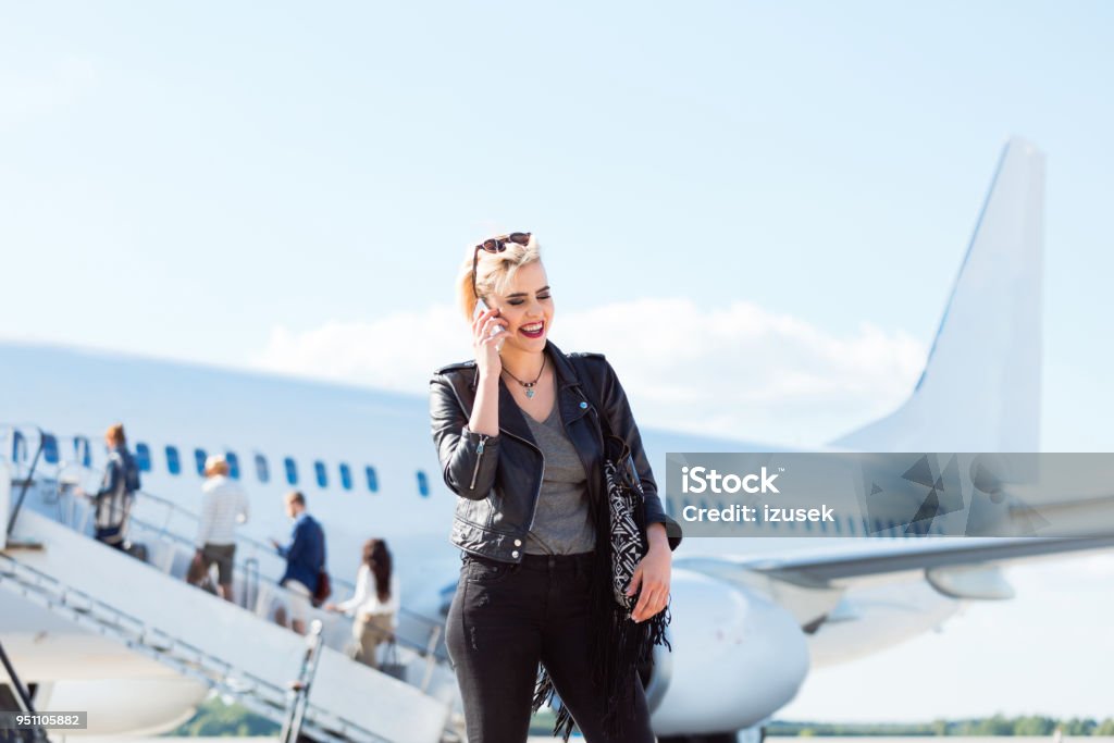 Beautiful woman on airport making phone call. Beautiful young woman standing in front of airplane and making a phone call. Female passenger standing on airport and talking on mobile phone. Adult Stock Photo