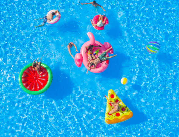 aerial: cheerful young friends having a watergun fight on floaties at pool party - bikini summer vacations looking down imagens e fotografias de stock