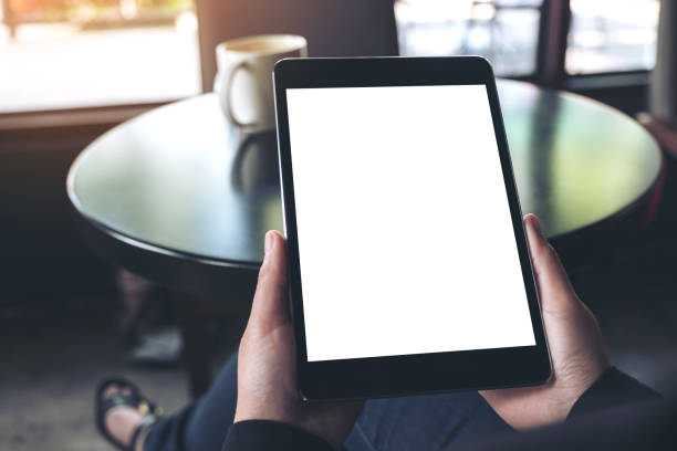 istock Mockup image of hands holding black tablet pc with blank white screen and coffee cup on table in cafe 951105956