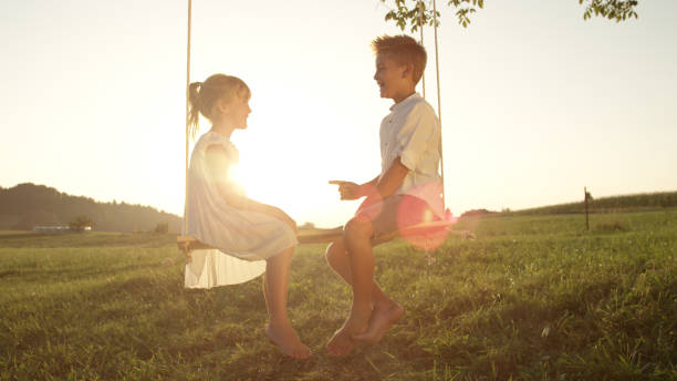 istock LENSE FLARE: Happy children sitting on swing facing each other on warm evening 951106010