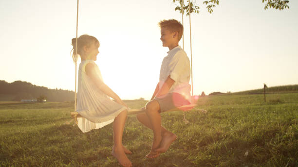 istock LENSE FLARE: Smiling children sitting on swing facing each other on warm evening 951106056