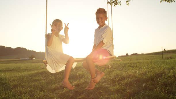 istock LENSE FLARE: Playful siblings sitting on a wooden swing posing for the camera 951106126