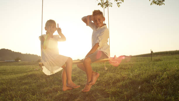 istock LENSE FLARE: Couple young children playfully posing for camera sitting on swing 951106156