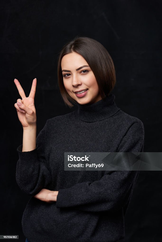 Hand counting - two fingers Hand counting - two fingers. Smiling woman in grey turtleneck sweater over dark background showing two fingers, V sign Peace Sign - Gesture Stock Photo