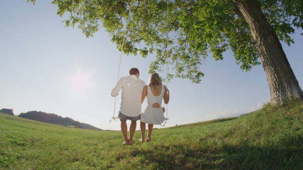 istock LENS FLARE: Happy couple swinging on swing under green tree on sunny spring day. 951106304