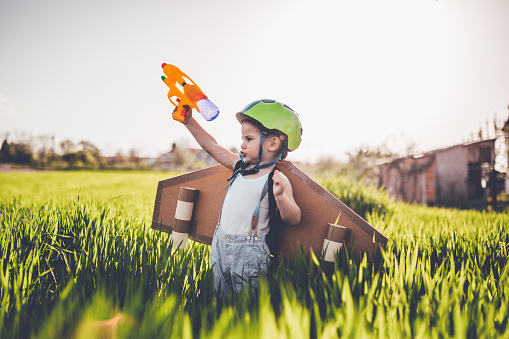 Little boy wearing aircraft wings and holding a gun on the meadow