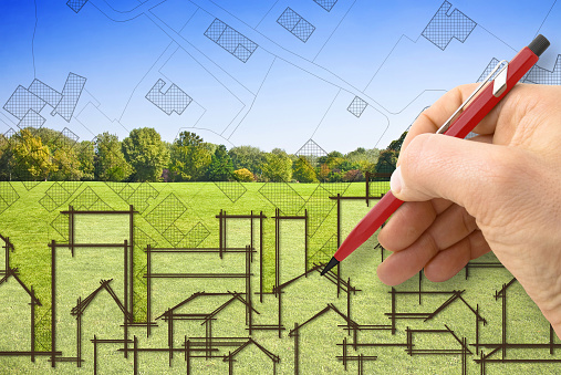 Cities and green spaces - concept image with architect drawing a residential district over a green mowed lawn with trees