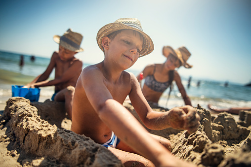 Brothers and sister are having fun building a sandcastle on a beach on a sunny summer day.\nNikon D810