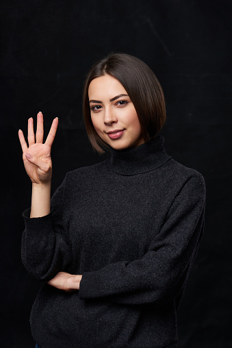 Hand counting - four fingers.Smiling woman in grey turtleneck sweater over dark background showing four fingers