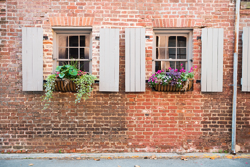 In Charleston, United States, a Southern travel destination, a residential brick home in the historic neighborhood has wooden shutters by the sides of the windows. Spring flowers fill the planter boxes on the exterior of the home.