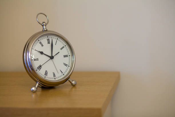 istock Table iron white clock on a wooden shelf against a blurred white wall 951121926