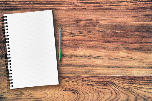 Blank notebook with pen are on top of wood table. Top view with copy space, flat lay.