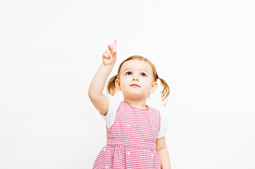 Portrait of a preschool toddler girl with ponytails pointing up, isolated on white studio background