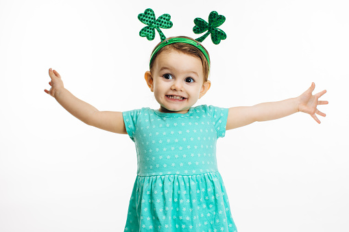An excited and happy small child with arms stretched out and St. Patrick's Day head decoration