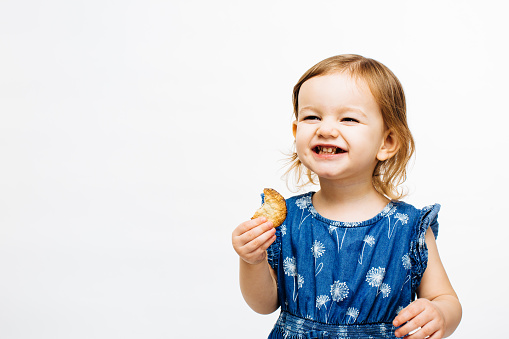 Smiling preschool girl eating a chocolate cookie, isolated on white background