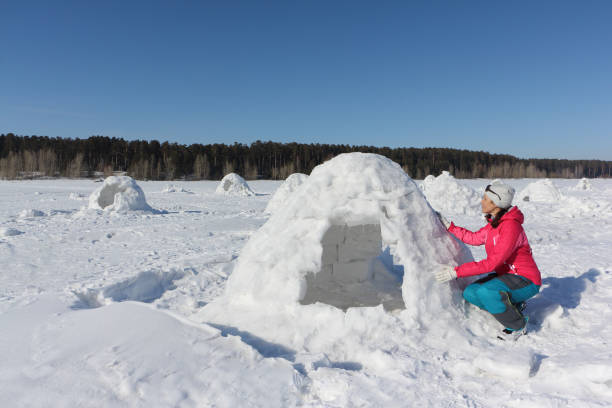 feliz mujer una chaqueta roja, construyendo un iglú en un claro de la nieve en el invierno - iglú fotografías e imágenes de stock