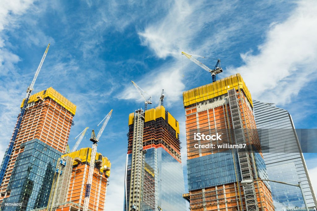 Skyscrapers construction site for modern buildings in New York Skyscrapers construction site for modern buildings in New York. Cranes and scaffolding used to build tall structures, blue sky on background. Construction Industry Stock Photo