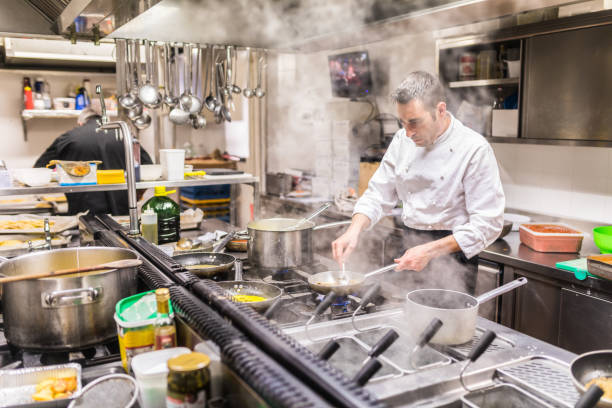 chef che cucina in una cucina di un ristorante, visto attraverso il vapore - silverware food and drink industry food service occupation dinner foto e immagini stock