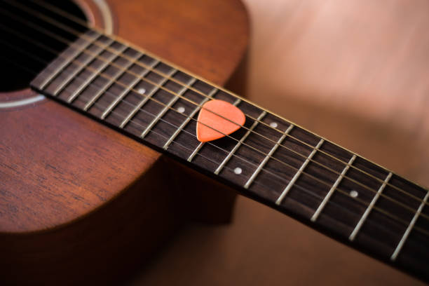 istock Orange guitar pick insert between string of acoustic guitar 951154098