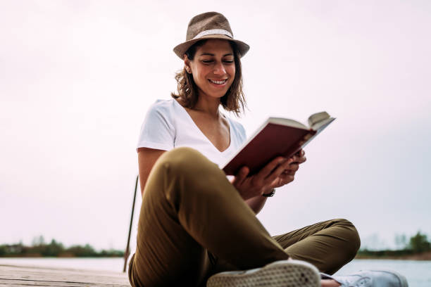 istock Smiling young lady reading book while sitting near water. 951158140