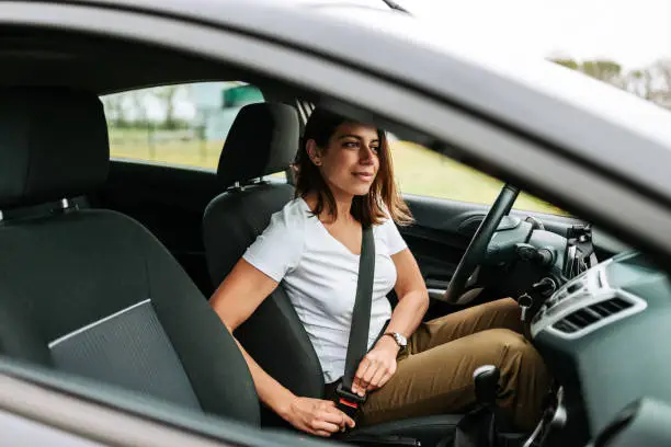 Photo of a business woman sitting in a car putting on her seat belt.