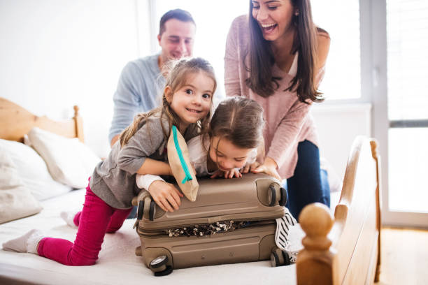 молодая семья с двумя детьми упаковывает вещи для отдыха. - family vacation стоковые фото и изображения