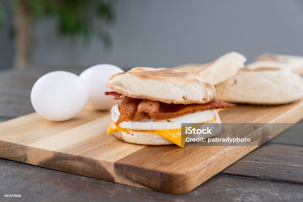 Bacon, Egg and Cheese Breakfast Sandwich Bacon, egg and cheese breakfast sandwich with english muffin on cutting board Egg - Food Stock Photo