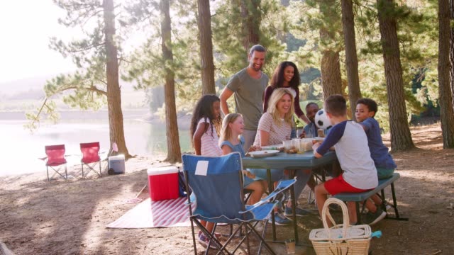 Family Enjoys Picnic As They Camp By Lake With Friends
