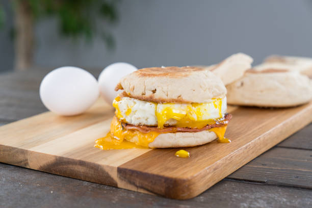 Canadian Bacon, Egg and Cheese Breakfast Sandwich with Yoke Canadian Bacon, egg and cheese breakfast sandwich with english muffin on cutting board with running yoke english muffin stock pictures, royalty-free photos & images