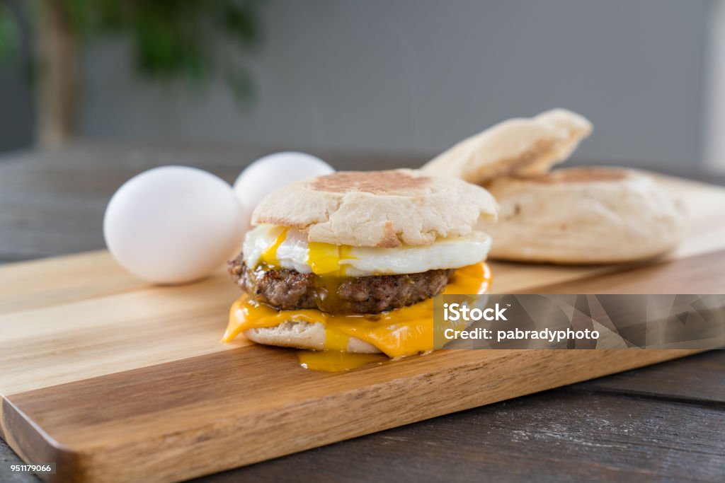 Sausage, Egg and Cheese Breakfast Sandwich with Yoke Sausage, egg and cheese breakfast sandwich with english muffin on cutting board with running yoke Sandwich Stock Photo