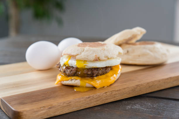 Sausage, Egg and Cheese Breakfast Sandwich with Yoke Sausage, egg and cheese breakfast sandwich with english muffin on cutting board with running yoke yoke stock pictures, royalty-free photos & images