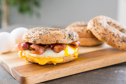 Bacon, egg and cheese breakfast sandwich with an everything bagel on cutting board