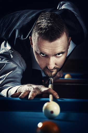 Close-up of billiard player ready for the shot. A young man is formally dressed and wears a white shirt and black vest.