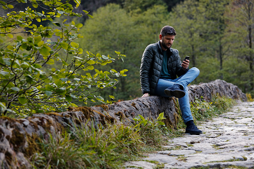 Modern young man with mobile phone in forest