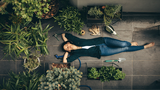 Young woman lying in her rooftop garden, having a rest from gardening