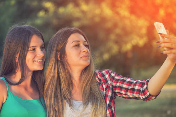 istock Two Beautiful Smiling Girls Taking Selfie Outdoors at Sunset 951224106