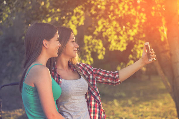 istock Two Beautiful Smiling Girls Taking Selfie Outdoors at Sunset 951225492