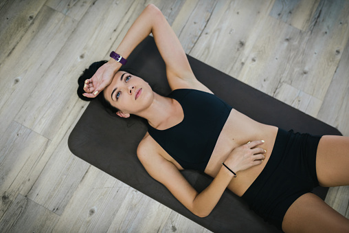 Attractive top view of fitness model lying on exercise mat. Overhead shot of fitness instructor wearing black sportswear, tired resting on mat on floor.