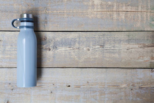 Stainless steel water bottle on wooden table Blue stainless steel, reusable drink container flat lay on a light brown wooden table, with copy space. Horizontal. bottled water on table stock pictures, royalty-free photos & images