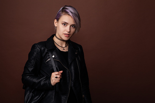 Close-up portrait of a beautiful young girl with blue hair in a black leather jacket in the studio on a brown background