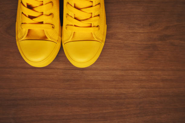 Stylish yellow sneakers on wooden background from above with copy space