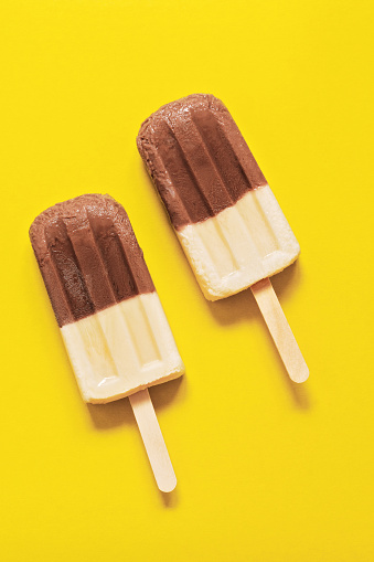 Two chocolate-vanilla ice-cream on a stick on a yellow background. Bright minimalism, the concept of summer