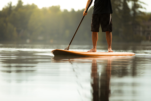 SUP Stand-up Paddleboard. Close-up on legs of a man paddleboarding