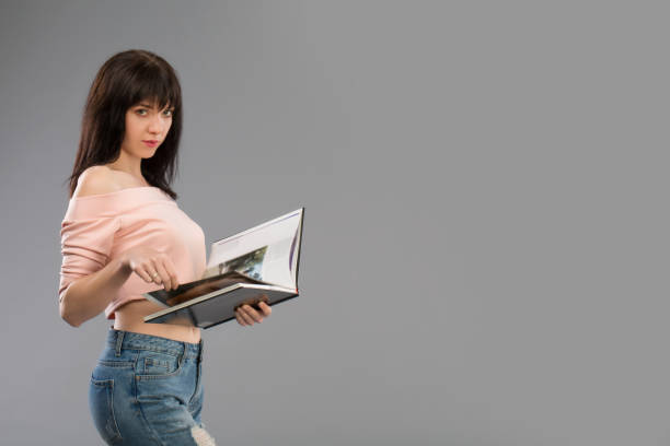 istock Serious attractive young woman or student reading a book as she holds it in both hands standing against a grey studio background 951270570