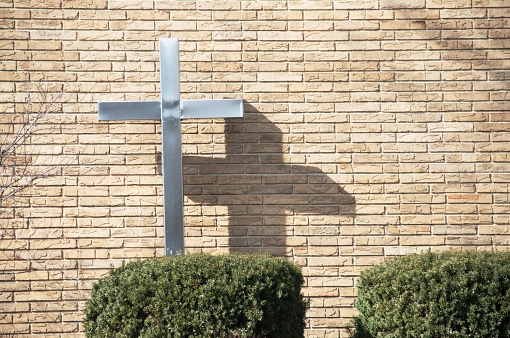 Aluminum cross and it shadow on brick church building.