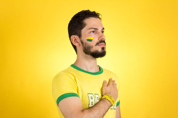 Brazilian supporter of National Team of football is listening to National anthem with hand on the chest. Soccer fan in action emotions: respect, pride. Supporter of Brazil National Team of football is listening to National anthem with hand on the chest. national anthem stock pictures, royalty-free photos & images