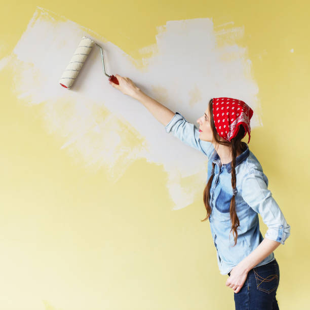 beautiful girl in red headband painting the wall with paint roller. - house painter paint roller yellow painting imagens e fotografias de stock